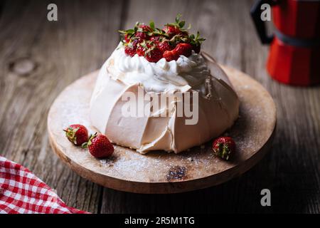 Pavlova-Kuchen mit Erdbeeren auf rustikalem Holztisch. Der Kuchen besteht aus Baiser und Schlagsahne Stockfoto
