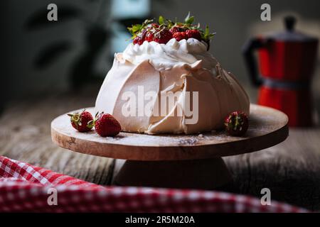 Pavlova-Kuchen mit Erdbeeren auf rustikalem Holztisch. Der Kuchen besteht aus Baiser und Schlagsahne Stockfoto