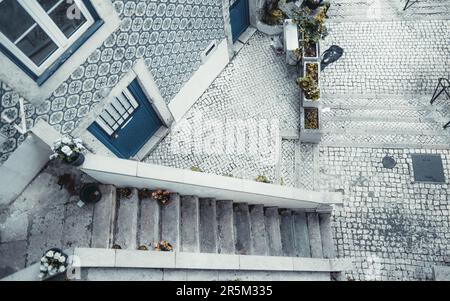 Bei einem Hochwinkel in Lissabon wird eine enge Treppe aufgenommen, die zu einer weißen kopfsteingepflasterten Straße führt. Verbunden mit der Treppe, zeigt die Fassade des Hauses exquis Stockfoto