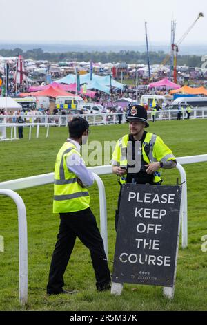 Epsom, Großbritannien. 3. Juni 2023. Am Tag des Epsom Derby stehen neben der Rennbahn Epsom Downs ein Polizist und ein Sicherheitsbeauftragter der Menge hinter einem Jockey Club-Schild. £150.000 wurden für zusätzliche Sicherheitsmaßnahmen ausgegeben, um einem geplanten Protest von Aktivisten von Animal Rising entgegenzuwirken, die Pferderennen als grausame und ausbeuterische Industrie ansehen. Die Polizei von Surrey berichtete, dass 31 Verhaftungen vorgenommen wurden, einschließlich 19 präventiven Verhaftungen. Kredit: Mark Kerrison/Alamy Live News Stockfoto