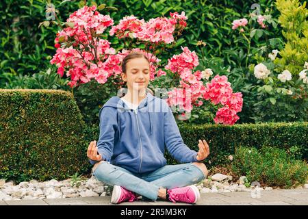 Außenporträt eines ruhigen jungen Mädchens, das im Park Meditation praktiziert Stockfoto