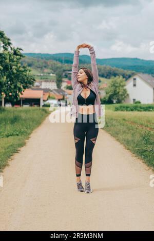 Außenporträt einer jungen, wunderschön sitzenden Frau in schwarzer Aktivbekleidung, Stretching von Sportlermodellen, Sportmode Stockfoto