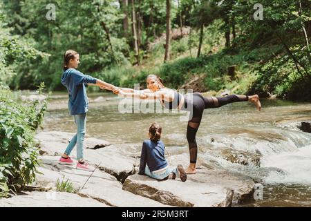 Eine junge, fitte Mutter, die mit ihren Töchtern und ihrer sportlichen Familie jung in der Natur trainiert Stockfoto