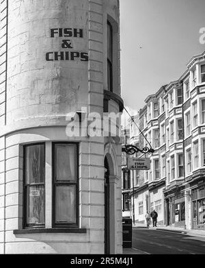 Ein Fischrestaurant in einem geschwungenen Gebäude auf einer geneigten Straße. Rote Backsteingebäude sind gegenüber von Geschäften und ein paar Schritte den Gehweg hinunter. Stockfoto