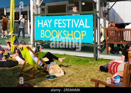 Die Leute entspannen sich in Liegestühlen und sitzen draußen auf dem Gras am Hay Festival Bookshop Schild am Hay on Wye in Sunshine 2023 Wales UK KATHY DEWITT Stockfoto