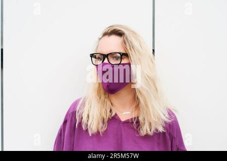 Outdoor-Modeporträt einer hübschen Frau mit violetter Bluse und Gesichtsmaske Stockfoto