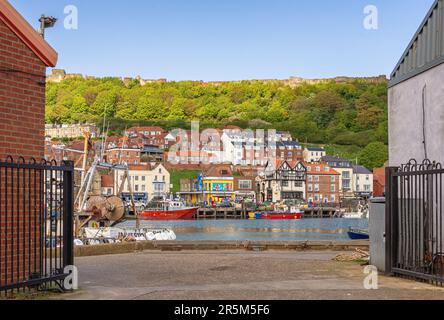 Scarborough Hafen und Stadt von zwei Gebäuden an einer Anlegestelle aus gesehen. Geschäfte und Restaurants säumen das Ufer und die Burgmauer befindet sich darüber. Stockfoto