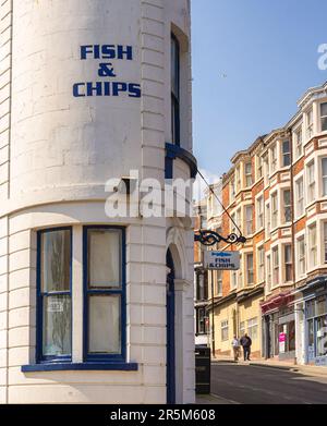 Ein Fischrestaurant in einem geschwungenen Gebäude auf einer geneigten Straße. Rote Backsteingebäude sind gegenüber von Geschäften und ein paar Schritte den Gehweg hinunter. Stockfoto