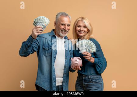 Seniorenpaar mit Geld und Sparschwein, isoliert auf Beige Stockfoto