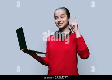 Glückliches, emotionales Teenager-Mädchen mit Laptop in den Händen auf grauem Hintergrund Stockfoto