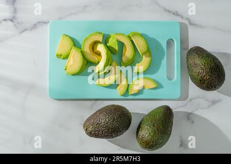 Avocado Nahaufnahme auf dem Küchentisch. Frische Avocado auf einem Schneidebrett auf Marmorhintergrund, flach liegend Stockfoto