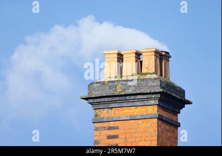 Holzrauch an einem blauen Himmel, der aus einem Ziegelkamin eines alten britischen Hauses weht Stockfoto
