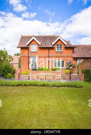 Großes englisches Landhaus und Garten im Sommer mit Rasen und Terrasse mit Teakholzgartenmöbeln Stockfoto