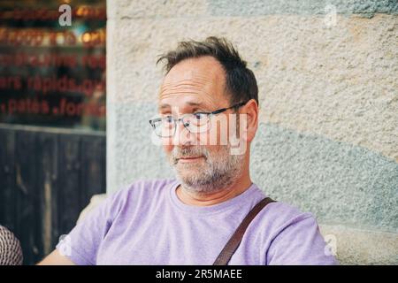 Lustiges Porträt eines überraschten Mannes mittleren Alters, der sich im Freien ausruht, lila T-Shirt und Brille trägt Stockfoto