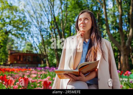 Junger weißer Landschaftsdesigner, der im Frühlingspark ein Notizbuch unter blühenden Blumen hält. Frau, die Ideen aufschreibt. Leerzeichen. Leerzeichen Stockfoto