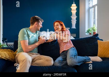 Glückliches junges Paar, das sich entspannt und sich mit Kaffee auf der Couch unterhält. Emotionale Verbindung in der Beziehung Stockfoto