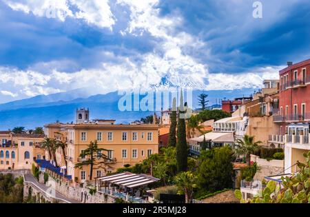 Taormina, Sizilien, Italien. Panoramablick über Taormina auf einem Hügel und den Ätna-Vulkan inmitten von Wolken am blauen Himmel. Beliebtes Touristenziel Stockfoto