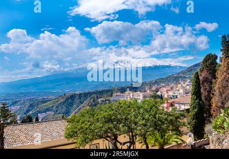 Taormina, Sizilien, Italien. Panoramablick über Taormina auf einem Hügel und den Ätna-Vulkan inmitten von Wolken am blauen Himmel. Beliebtes Touristenziel Stockfoto