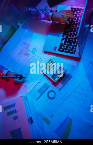 Oberansicht einer modernen Frau mit Taschenrechner, Dokumenten und Laptop zur Erkundung von Diagrammen. Stockfoto