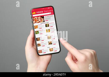Lebensmittellieferservice. Frau wählt Gericht aus der Speisekarte vor Ort mit Smartphone auf grauem Hintergrund, Nahaufnahme Stockfoto