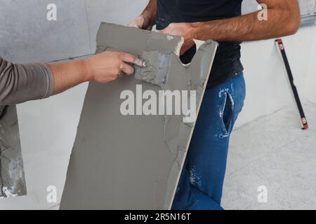 Arbeiter, die Zement auf Fliesen in Innenräumen anwenden, schließen Stockfoto