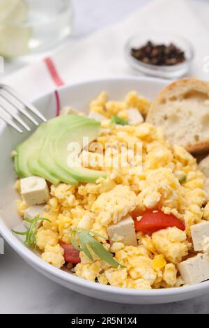 Schüssel mit köstlichem Rührei, Tofu und Avocado auf weißem Tisch, Nahaufnahme Stockfoto