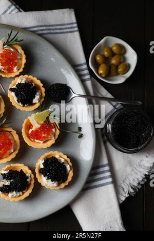 Köstliche Törtchen mit rotem und schwarzem Kaviar, serviert auf einem dunklen Tisch, flach liegend Stockfoto