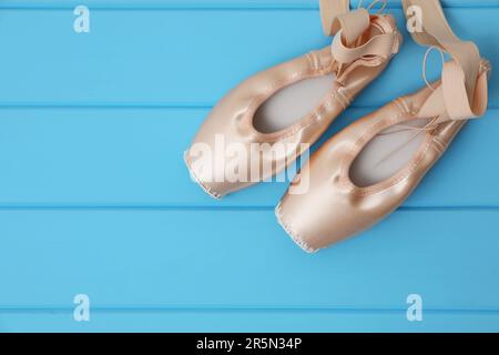 Wunderschöne beige Ballettschuhe mit niedlichen Bändern auf hellblauem Holztisch, Blick von oben. Platz für Text Stockfoto