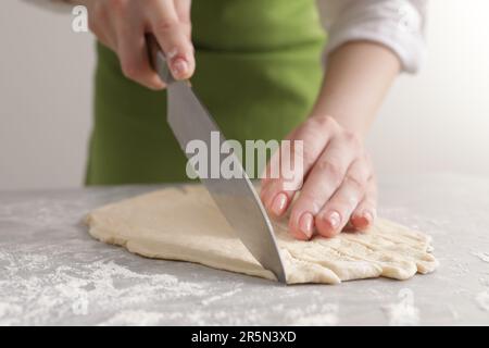 Frau schneidet Teig auf einem hellgrauen Marmortisch, Nahaufnahme. Ich koche Grissini Stockfoto