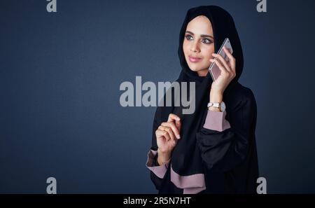 Sich mit Menschen zu verbinden, die wichtig sind. Studiofoto einer jungen Frau, die eine Burka trägt und ein Handy benutzt, vor grauem Hintergrund. Stockfoto