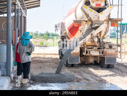 Betonmischwagen gießt Beton auf dem Boden auf der Baustelle und Arbeiter wartet auf Estrich. Stockfoto