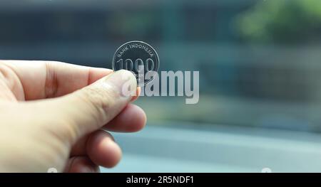 Eintausend Rupiah-Münzen, eine Hand mit einer Rupiah-Münzen isoliert auf einem verschwommenen Hintergrund. Indonesische Rupiah-Währung Stockfoto