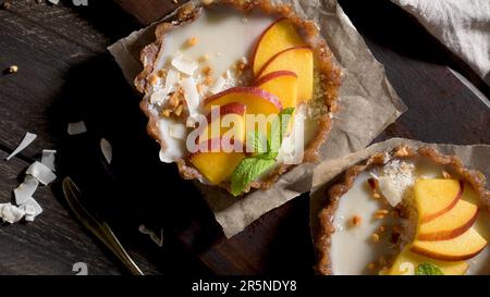 Vegane Pfirsichtörtchen mit geriebener Kokosnuss und knusprigen Erdnüssen. Obstkuchen. Dattel, Walnuss-, Mandel- und Haselnussbasis. Stockfoto