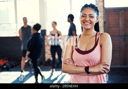 Übung erzeugt fröhliche Stimmungen. Porträt einer fröhlichen jungen Frau, die mit zusammengeklappten Armen in die Kamera schaut, bevor sie im Fitnessstudio trainiert Stockfoto