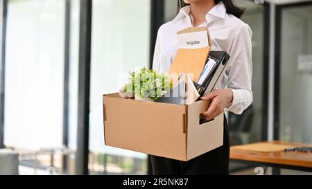 Zugeschnittenes Bild einer Büroangestellten steht im Büro und hält ihren Karton mit Sachen und ihrem Kündigungsschreiben in der Hand. Gefeuert, arbeitslos Stockfoto