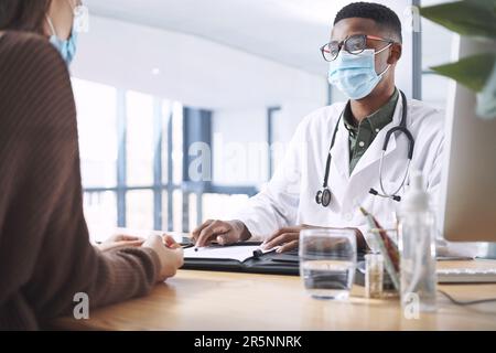 Sind Sie bereit fortzufahren? Ein junger Arzt, der bei seinem Patienten sitzt und seine Gesichtsmaske während einer Sprechstunde in der Klinik trägt. Stockfoto