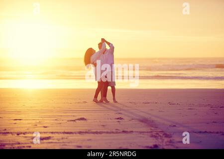 Sonnengeküsste Liebhaber. Die volle Länge eines liebevollen, erwachsenen Paares, das bei Sonnenuntergang am Strand tanzt. Stockfoto