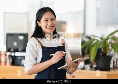 Asiatischer Cafe-Besitzer oder Barista, der mit einem Lächeln im Café steht. Frau, Inhaber eines kleinen Unternehmens in der Gastronomie Stockfoto