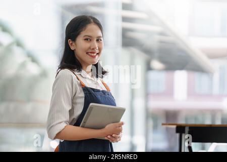 Asiatischer Cafe-Besitzer oder Barista, der mit einem Lächeln im Café steht. Frau, Inhaber eines kleinen Unternehmens in der Gastronomie Stockfoto
