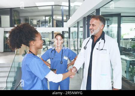 Herzlichen Glückwunsch zu Ihrer Assistenzzeit. Eine attraktive junge Krankenschwester, die in der Klinik steht und einem Arzt die Hand schüttelt. Stockfoto
