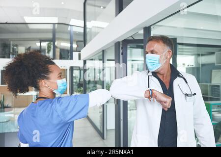 Auf dem Weg, um die Ausbreitung von Covid zu verhindern. Ein gut aussehender, reifer Arzt, der steht und seinen Ellbogen als Begrüßung in der Klinik anschlägt. Stockfoto