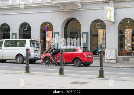 wien, österreich. Am 1. april 2023 radelt ein Radfahrer vorbei und überholt ein rotes Auto auf einer wiener Straße Stockfoto