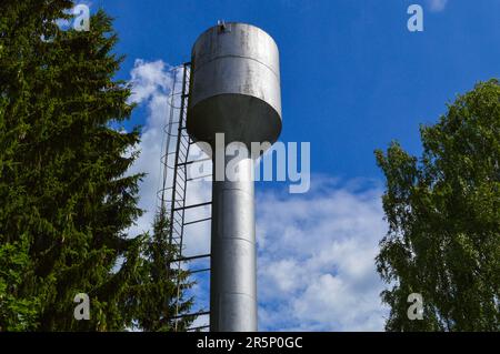 Großer rostfreier Wasserturm aus Eisen, glänzend, aus Metall, für die Versorgung von Wasser mit großer Kapazität, Fass gegen den blauen Himmel und Bäume. Stockfoto