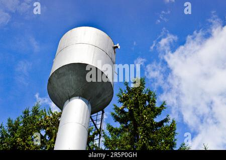 Großer rostfreier Wasserturm aus Eisen, glänzend, aus Metall, für die Versorgung von Wasser mit großer Kapazität, Fass gegen den blauen Himmel und Bäume. Stockfoto