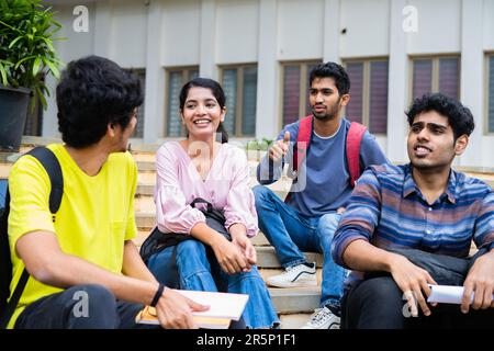 Gruppe glücklicher Schüler, die sich unterhalten, während sie auf dem Campus des Colleges sitzen - Konzept von Freundschaft, Pausenzeit und Kommunikation Stockfoto