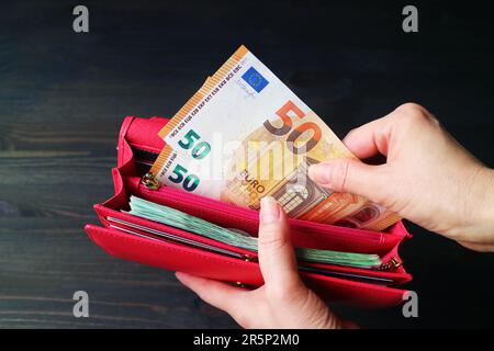 Nahaufnahme der Hand einer Frau, die einen Haufen Euro-Banknoten in einer roten Brieftasche hält Stockfoto