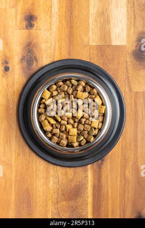 Trockenes Kibble-Tierfutter. Hunde- oder Katzenfutter in der Schüssel auf dem Holztisch. Draufsicht. Stockfoto