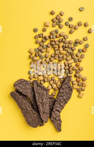 Trockenes Kibble-Tierfutter und Trockenfleisch. Hunde- oder Katzenfutter auf gelbem Hintergrund. Draufsicht. Stockfoto
