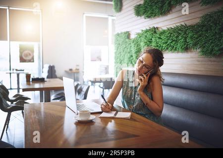 Und die Kunden kommen immer wieder. Eine junge Frau, die während der Arbeit in einem Café einen Laptop und ein Smartphone verwendet. Stockfoto