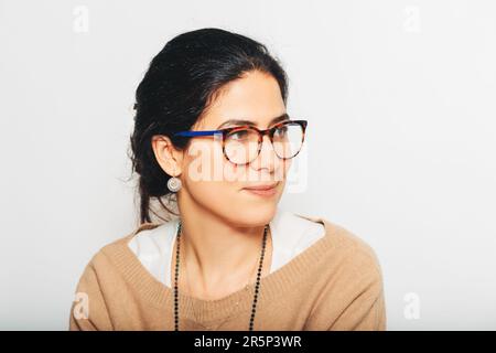 Studioporträt einer schönen braunen Frau, die eine Brille trägt, zur Seite blickt, auf weißem Hintergrund posiert Stockfoto